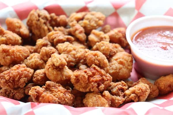 Buffalo boneless wings served with celery sticks and ranch dressing on red-and-white checkered paper in a green basket.