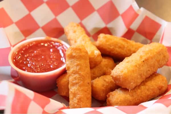 Golden fried mozzarella sticks served with a side of marinara sauce in a red-and-white checkered paper-lined basket.