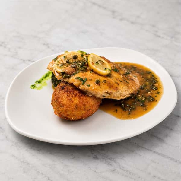 Chicken Francese with lemon caper butter sauce served alongside a golden crab cake at Local on North, featuring coastal-inspired Southern flavors in Canton and Marietta.