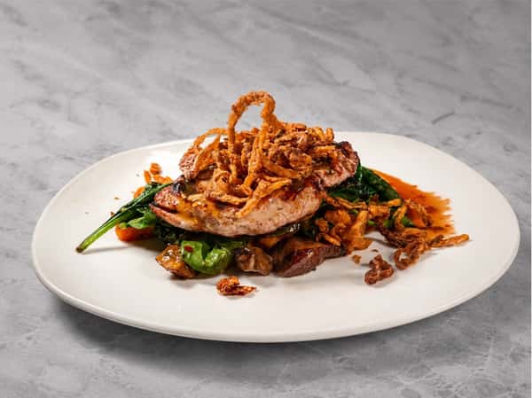 Grilled pork ribeye topped with crispy onions and served with seasonal vegetables in a savory pan sauce at Local on North, offering chef-driven Southern-inspired cuisine.