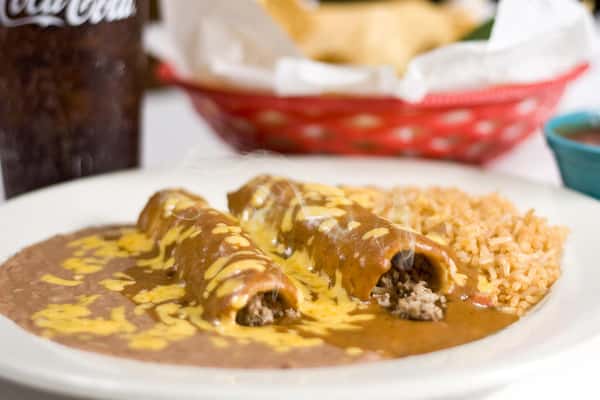 Taquitos covered in sauce and cheese with a side of rice