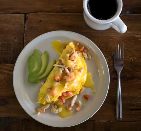 Omelet topped with melted cheese and salsa, served with avocado.