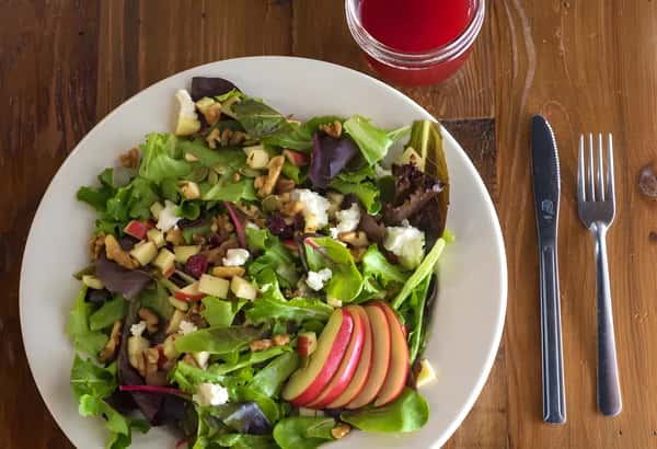 Fresh mixed green salad topped with grilled chicken, apples, nuts, and vegetables.