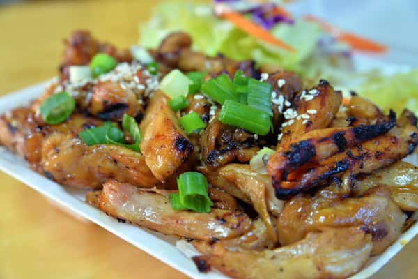 A close-up of freshly grilled teriyaki chicken glazed in a rich, glossy sauce, topped with chopped green onions and served over a bed of rice, showcasing a savory and mouthwatering finish.