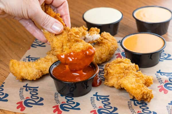 Hand dipping a chicken tender into a cup of sauce