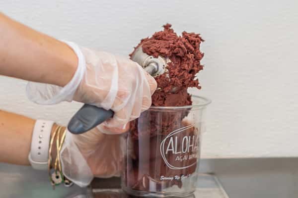A gloved hand scoops dark red acai sorbet.