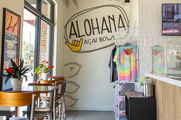 ALOHAHA Açaí Bowls interior with wall logo, colorful merchandise, and window seating with plants and natural light.