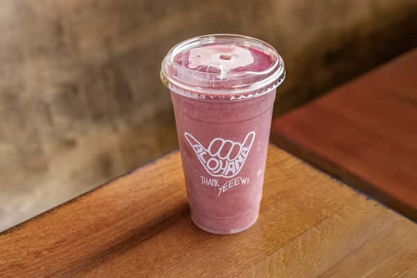 A thick, vibrant purple smoothie—likely made with berries or acai—is served in a clear cup branded with the "Alohaha" logo, sitting on a wooden table.