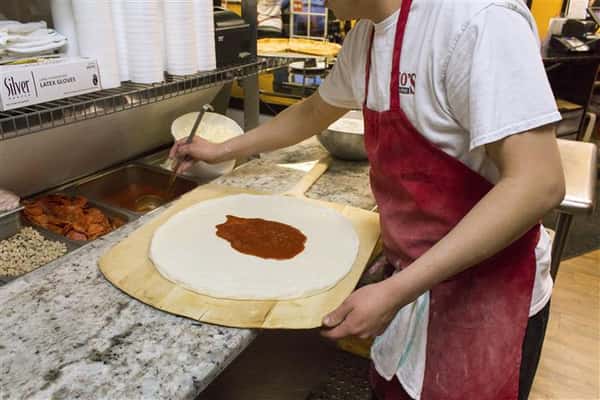 PIzza cook putting sauce on dough on pizza peel