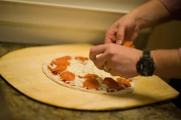 Pizza cook placing pepperoni over mozzarella on dough