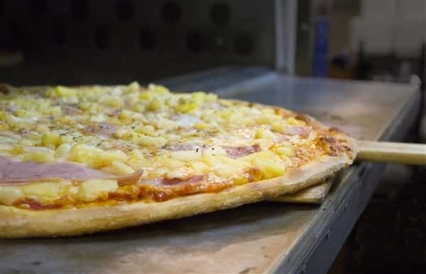 Pineapple and ham pizza coming out of oven