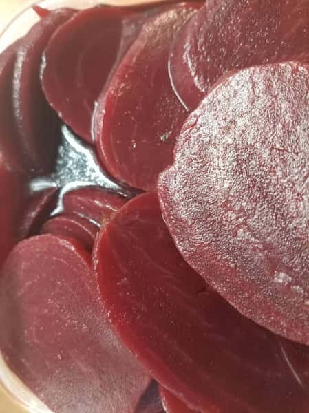 Close-up of glossy sliced pickled beets with deep red color and smooth texture, prepared as a tangy salad or sandwich topping.