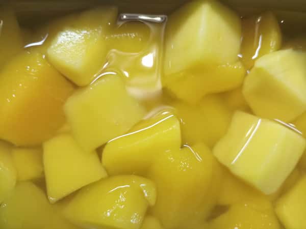 Close-up of bright yellow diced fruit pieces in syrup, likely canned mango or pineapple, glistening in liquid for dessert or tropical fruit topping.