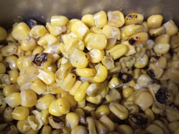 Roasted corn kernels with light char marks in a food prep container, a flavorful topping often used for salads, bowls, or street-style corn dishes.