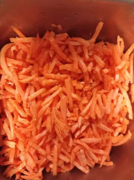 Freshly shredded carrots in a container, bright orange and ready for salad toppings, slaws, or healthy vegetable dishes.
