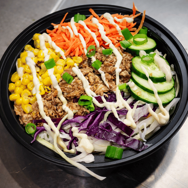 Healthy rice bowl with shredded chicken, charred corn, shredded carrots, purple cabbage, cucumber slices, and creamy sauce drizzle.