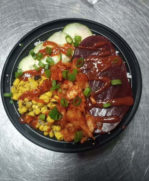 Korean-inspired rice bowl with pickled beets, kimchi, charred corn, cucumber slices, green onions, and spicy sauce over rice.
