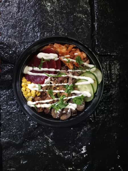 BBQ rice bowl with smoked pulled pork, roasted corn, sautéed mushrooms, cucumber slices, pickled beets, kimchi, and fresh herbs, finished with a creamy sauce drizzle.