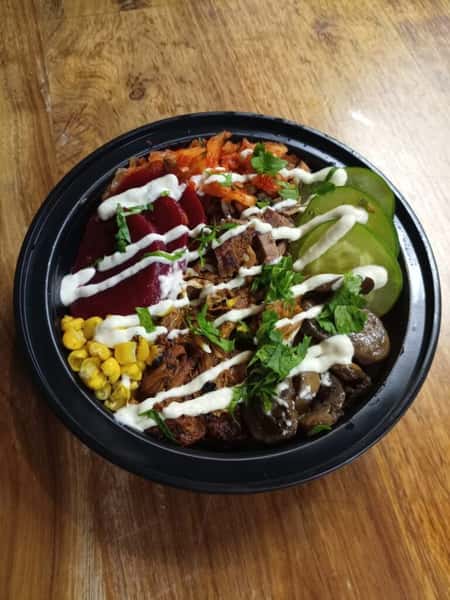 Fresh Korean-style rice bowl with roasted corn, pickled beets, cucumbers, kimchi, mushrooms, and grilled meat topped with creamy dressing.