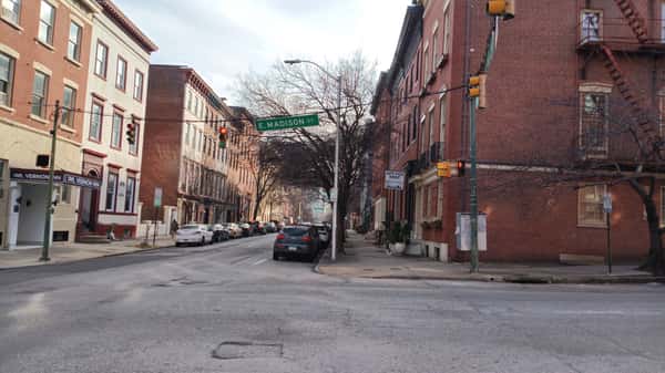 Historic city intersection with brick row houses, parked cars, and a green 'E. Madison St' street sign in a quiet urban neighborhood.