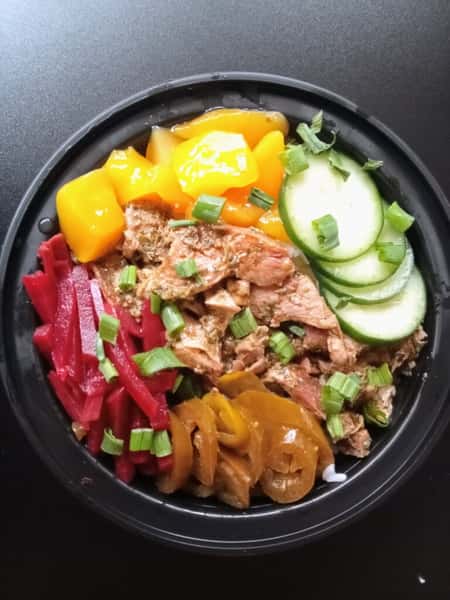 Colorful rice bowl with shredded chicken, pickled red vegetables, diced mango, cucumber slices, jalapeños, and green onions in a black bowl.