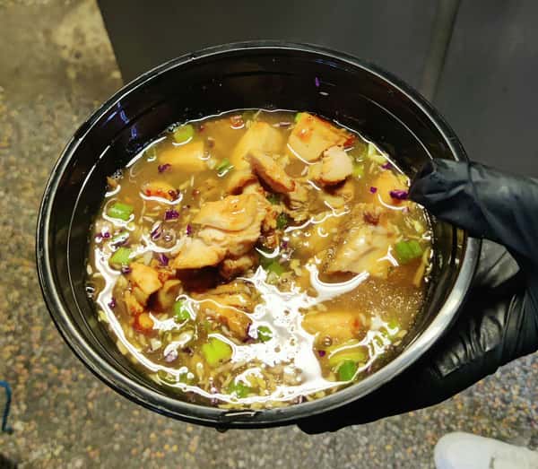 Hearty chicken soup with shredded smoked chicken, rice, scallions, and vegetables in a savory broth, served in a black bowl in a casual restaurant kitchen.