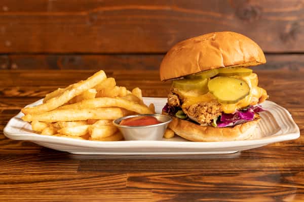 Crispy fried chicken topped with melted cheddar, zesty pickles, and a crunchy, sweet-and-spicy coleslaw, finished with a drizzle of chili aioli, all on a fresh house-made bun.