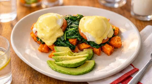 Eggs Benedict with hollandaise sauce, spinach, sweet potato hash, and sliced avocado.