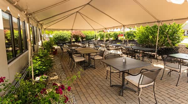Outdoor patio dining area under a white tent with black metal tables and chairs on a brick paver floor.