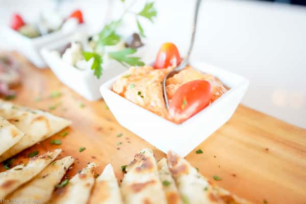 Roasted red pepper dip garnished with cherry tomato and parsley, served with warm pita bread on wooden board