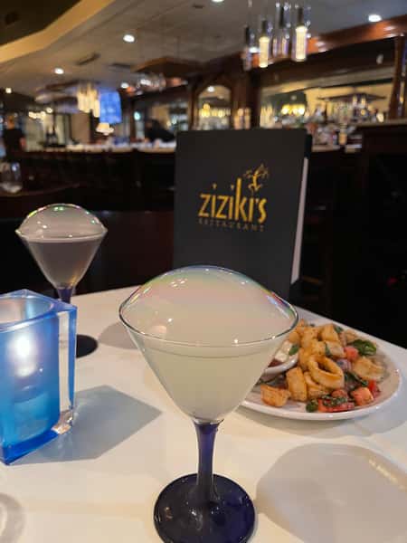 Two martinis topped with smoke bubbles on a table at Ziziki's Restaurant, with calamari and a blue candle in view