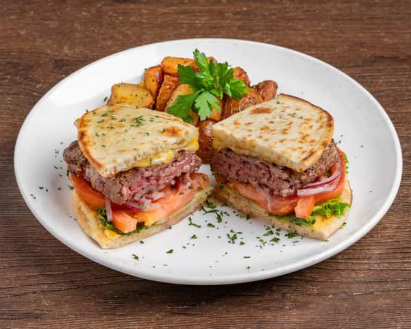 Burger sliders on toasted flatbread with lettuce, tomato, red onion, melted cheese, and roasted potatoes on a white plate