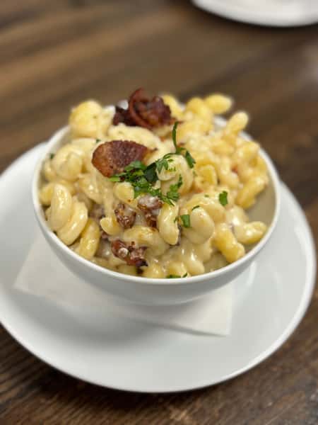 Creamy bacon mac and cheese topped with parsley, served in a white bowl on a wooden table at Jonathan the rub.