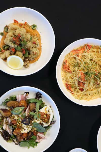 Assorted restaurant dishes including fried calamari, lobster pasta, and a fresh salad with prosciutto and burrata