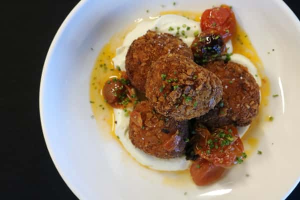 crispy fried croquettes with creamy aioli and blistered cherry tomatoes on a white plate