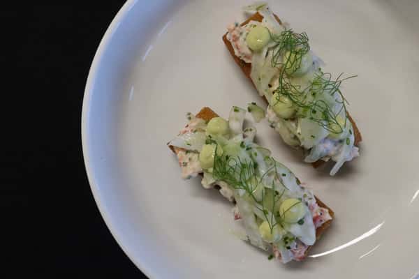 Elegant seafood appetizer with lobster salad on toasted bread topped with herbs and creamy sauce