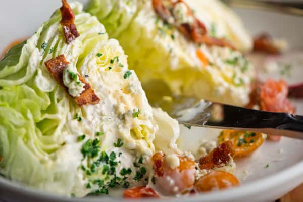 Classic iceberg wedge salad topped with creamy blue cheese dressing, crispy bacon, fresh herbs, and cherry tomatoes.