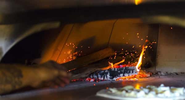 Hands placing wood into wood fired pizza oven