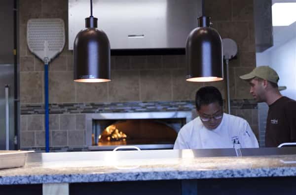 Chef in kitchen behind counter, in front of pizza oven