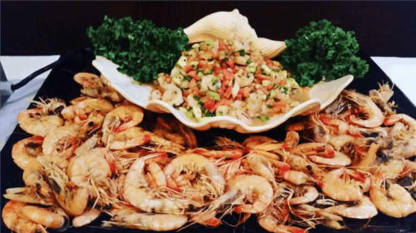 Catering display of a large plate with unpeeled shrimp and ceviche garnished with greens