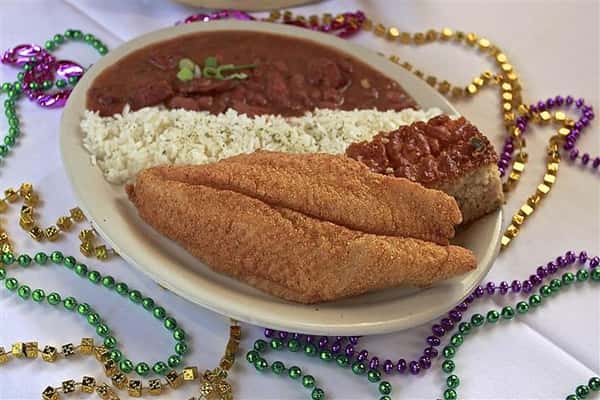 Fried fish, white rice, red beans on a plate on a table decorated with mardi gras beads