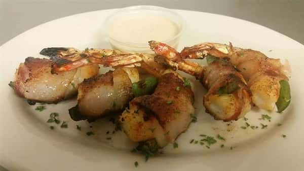 bacon wrapped shrimp garnished with green and a side of dipping sauce