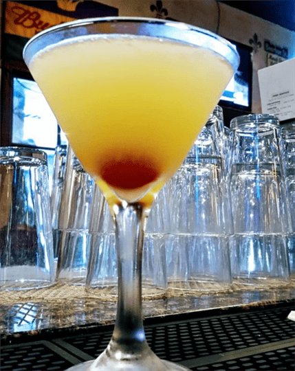 Yellow martini with a cherry in a martini glass on a bar top
