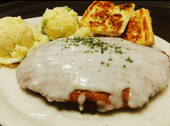 Fried filet of seafood topped with a cream sauce and a green garnish, served with a slide of mashed potatoes and sliced loaf of bread