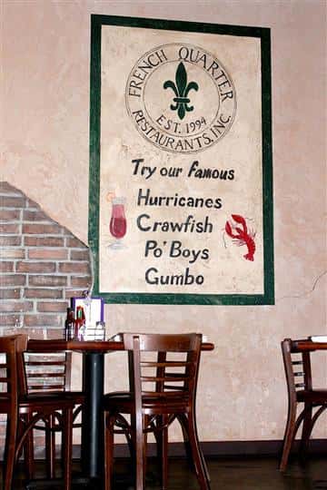 Interior of resturant with a few tables and chairs and a sign on the wall that says "try our famous hurricanes, crawfish, po' boys and gumbo"