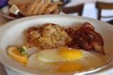 Plate with sunny side up eggs, bacon, hash, and sliced toast in the background