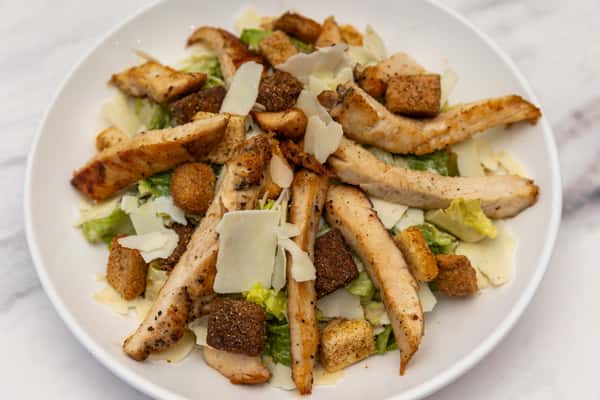grilled chicken salad with sliced chicken breast, croutons, and shaved parmesan over fresh greens