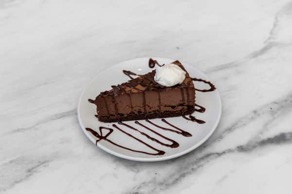rich chocolate cake slice topped with whipped cream and chocolate drizzle on a marble surface