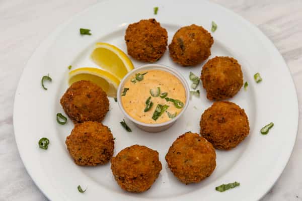 crispy crab arancini served with creamy dipping sauce and lemon wedges on a white plate