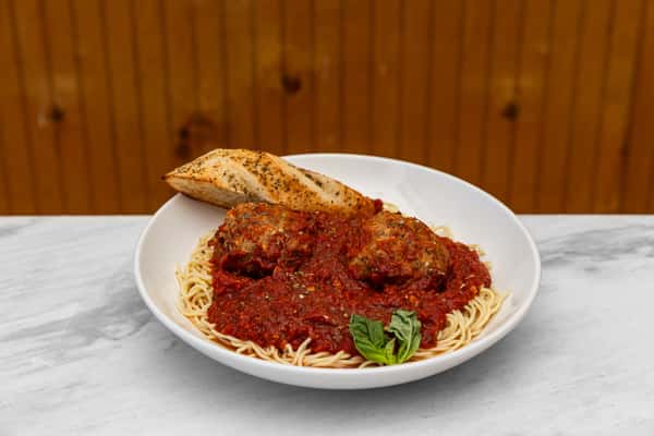 spaghetti and meatballs in marinara sauce garnished with herbs and served with garlic bread